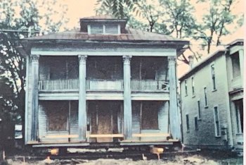 An old two-story Brackenridge House, elevated on wooden beams for structural work, features a columned porch.