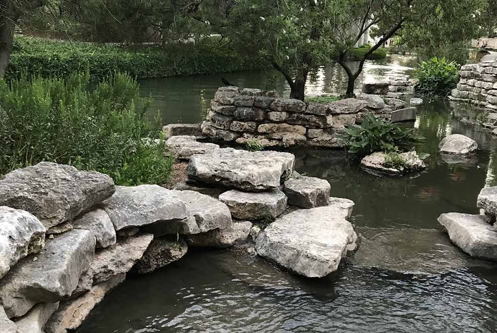 Large limestone rocks arranged as steps leading across a shallow, calm stream at a San Antonio, TX, bed and breakfast.