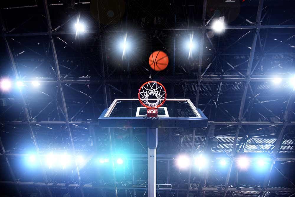 A basketball travels through the air toward a hoop in a brightly lit arena, reminiscent of upcoming events in San Antonio.