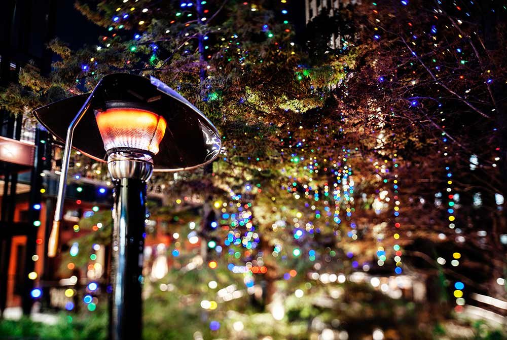 A lit outdoor patio heater stands in front of a tree decorated with colorful holiday lights at night, highlighting upcoming events in San Antonio.