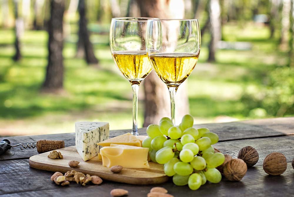 Two glasses of white wine sitting on a wooden table with a cheese board, grapes, and walnuts, perfect for things to do in San Antonio Texas.