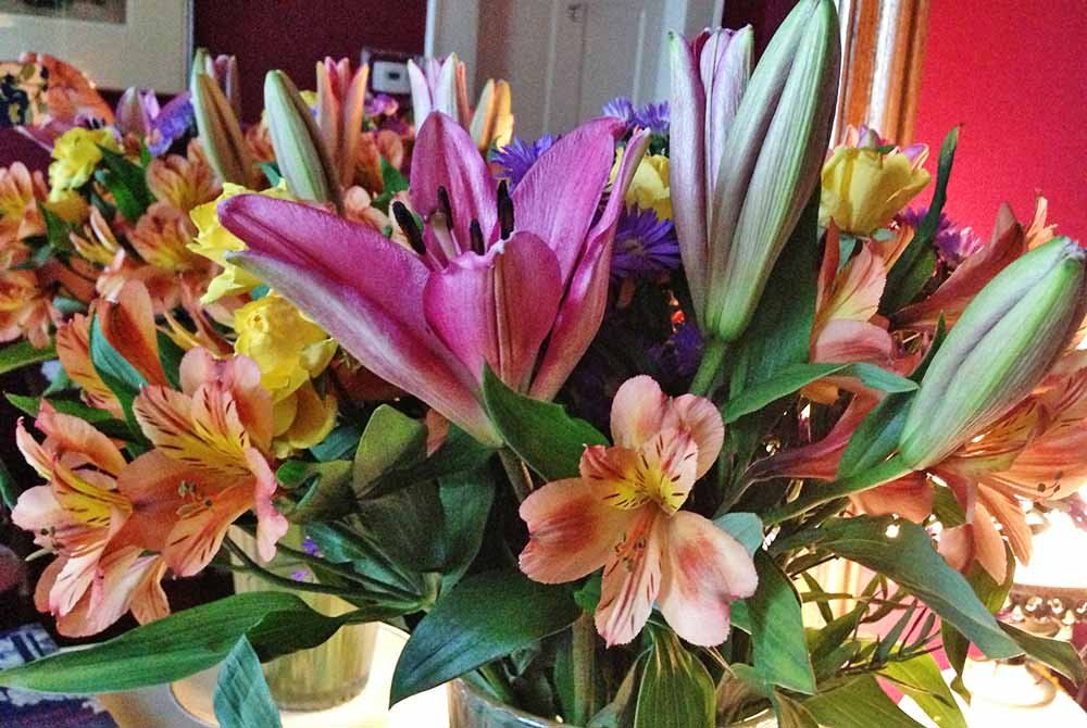 A colorful floral bouquet of pink lilies, orange alstroemeria, and yellow flowers in a glass vase, perfect for San Antonio getaway packages.