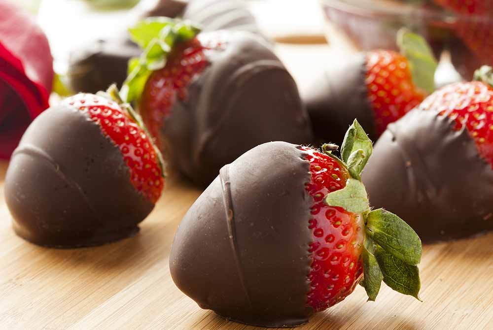 Several fresh strawberries partially dipped in dark chocolate arranged on a wooden surface, a sweet treat to enjoy during San Antonio getaway packages.