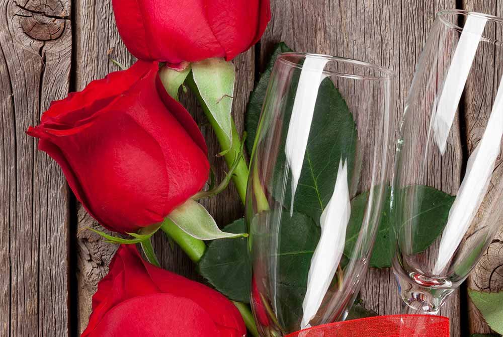 Three red roses and two empty champagne flutes on a rustic wooden surface, reminiscent of San Antonio getaway packages.