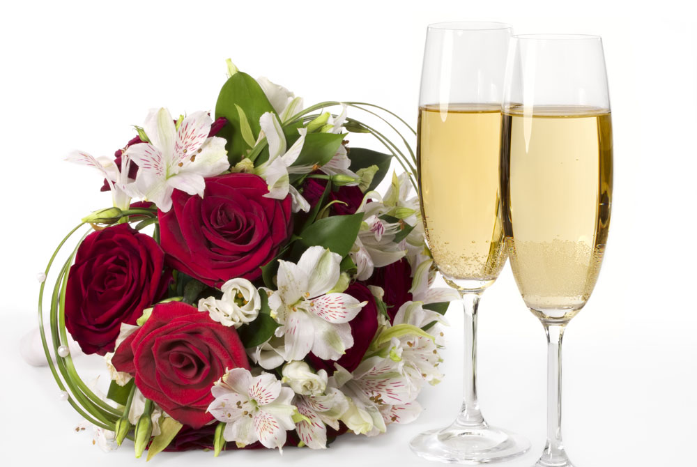 A bouquet of red roses and white alstroemeria next to two flutes of champagne, perfect for San Antonio getaway packages.